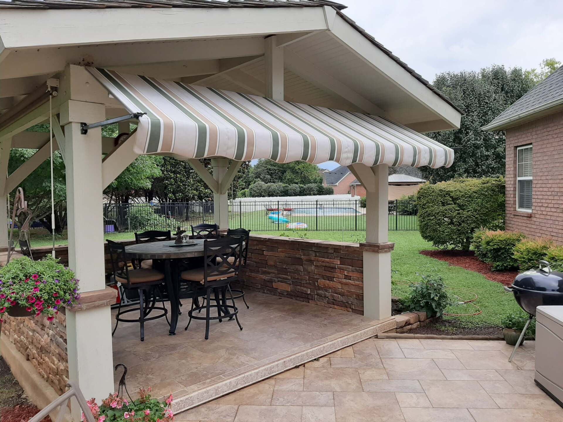 A patio with a table and chairs under a canopy with a striped awning.