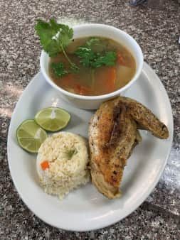 Bowl of soup, roasted chicken, rice, and lime wedges on a plate. Garnished with cilantro.