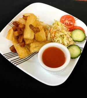 Fried cassava with a side of coleslaw, tomato, cucumber, and dipping sauce on a white plate.