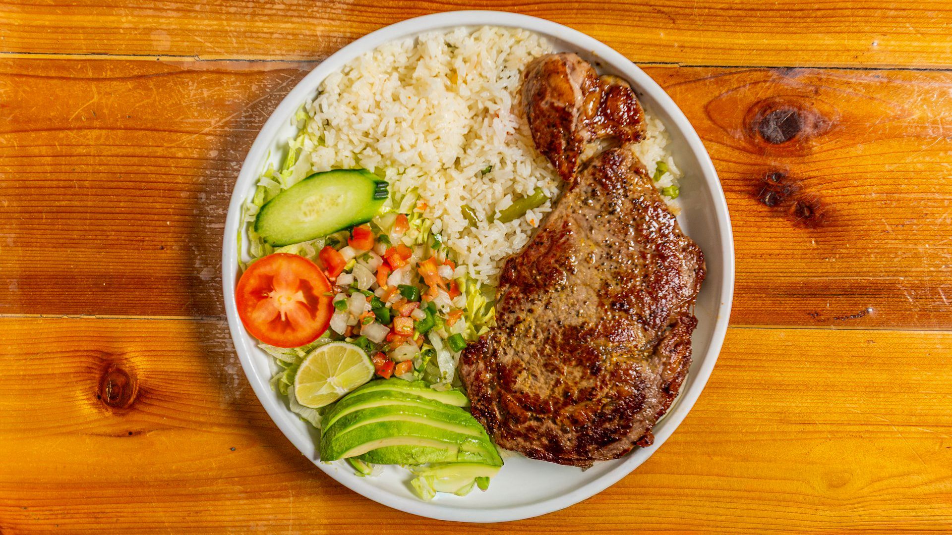 Plate with rice, meat, salad, avocado, tomato, and lime.