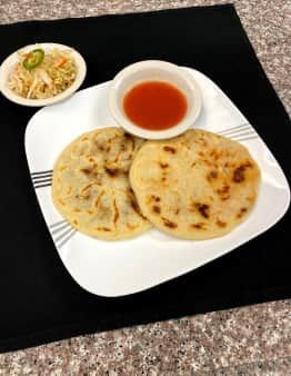 Two pupusas, red sauce, and curtido on a plate. Black background.