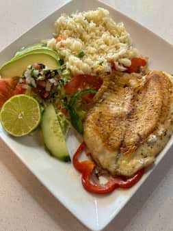 Grilled chicken breast with rice, avocado, and vegetables on a white plate.