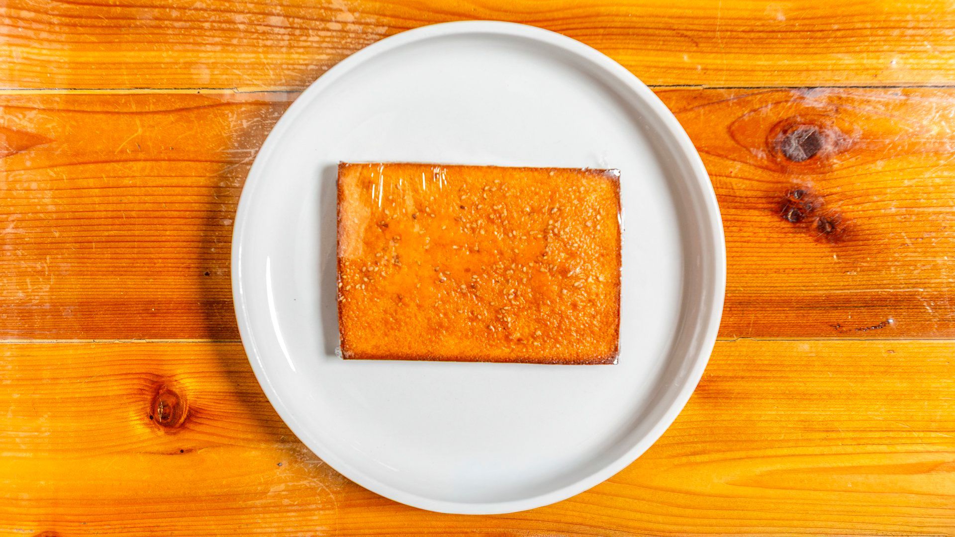 Rectangular slice of tofu on a white plate, set on a wooden table.