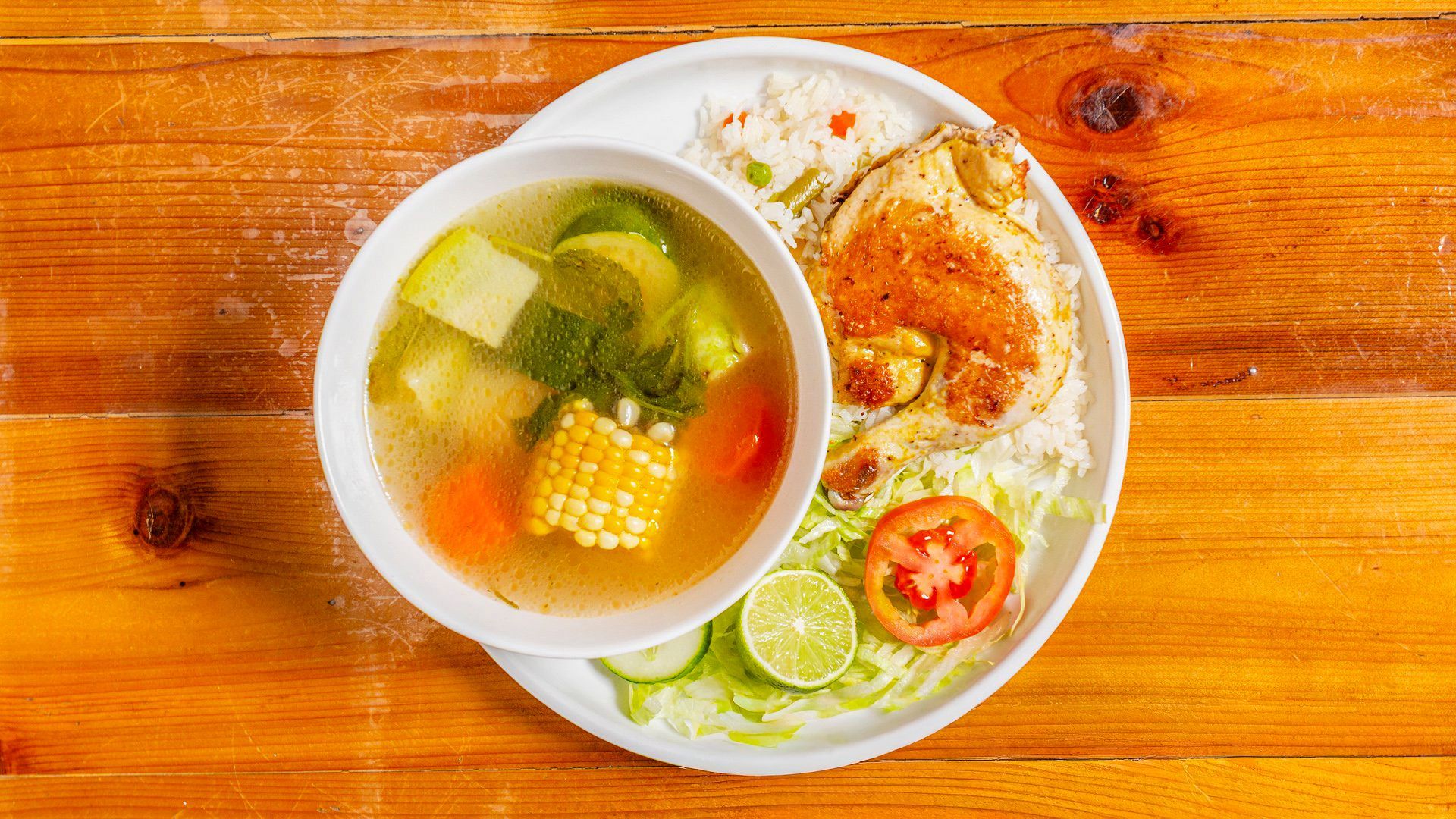 Soup, rice, and chicken on a white plate, with a wooden background.