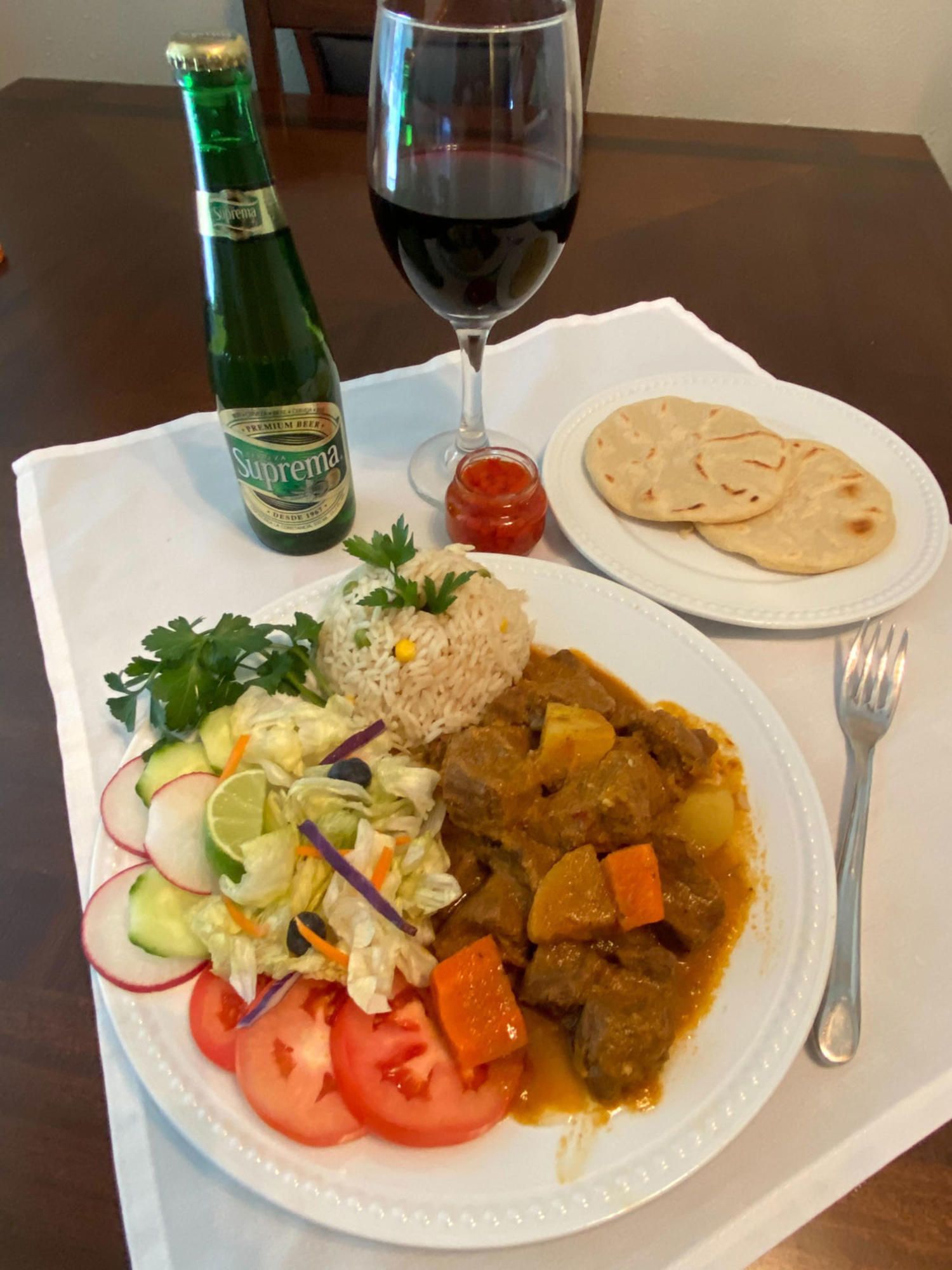Plate of beef stew with rice, salad, bread, and drinks.