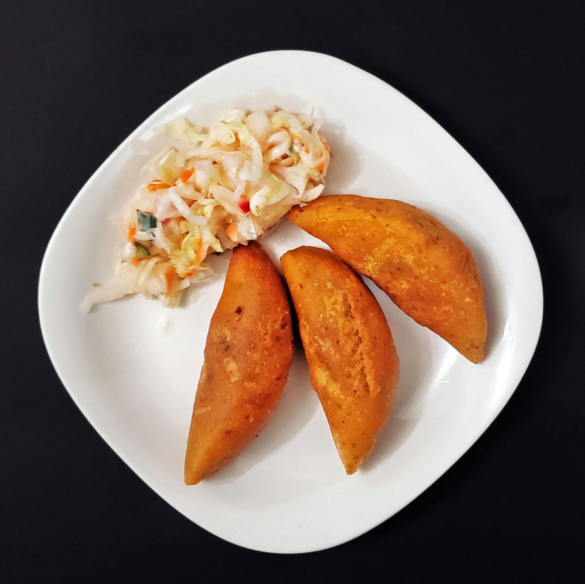 Plate with three fried pastries and a side of coleslaw.