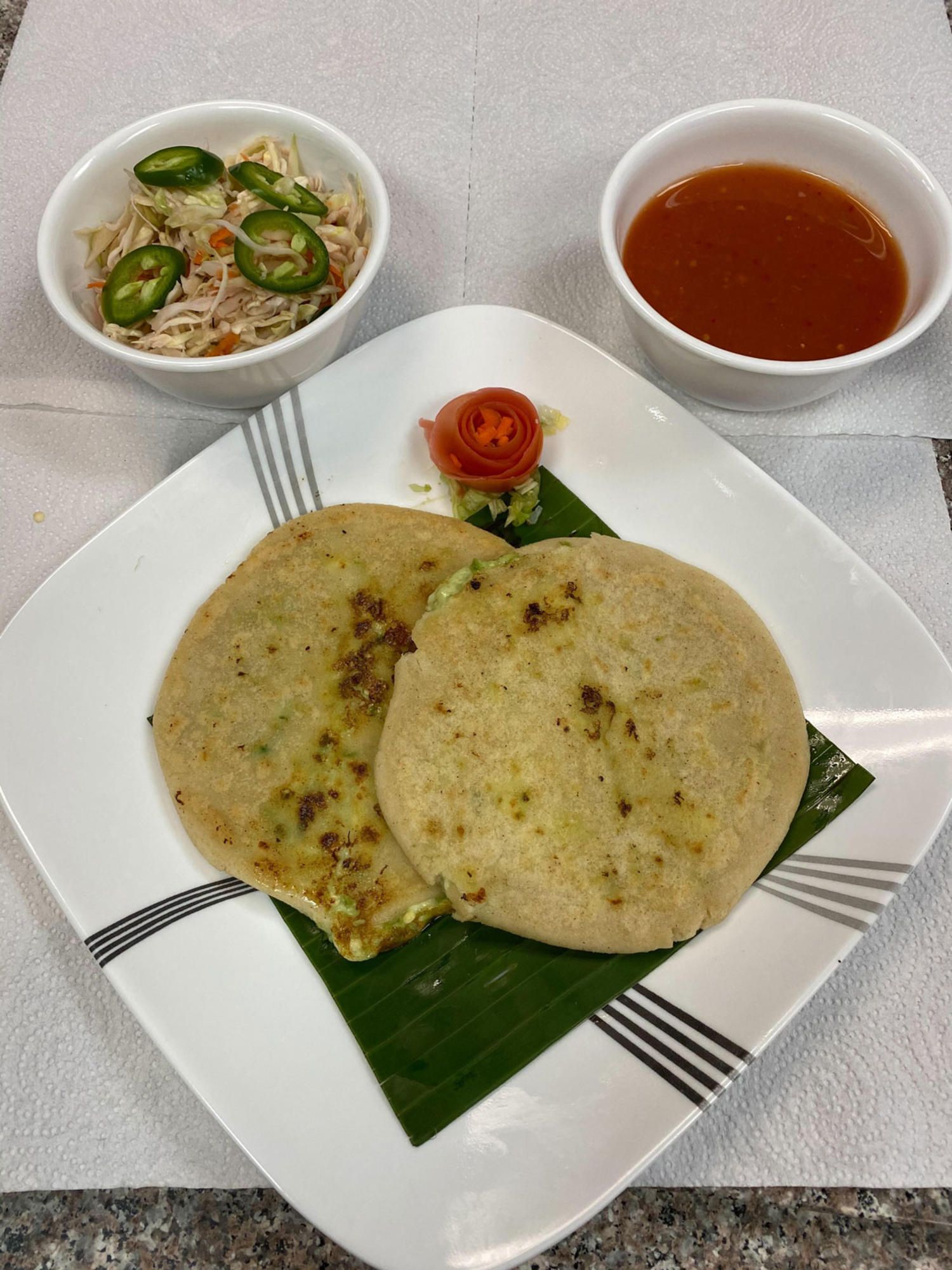 Two pupusas on a plate with curtido, salsa, and a tomato garnish.