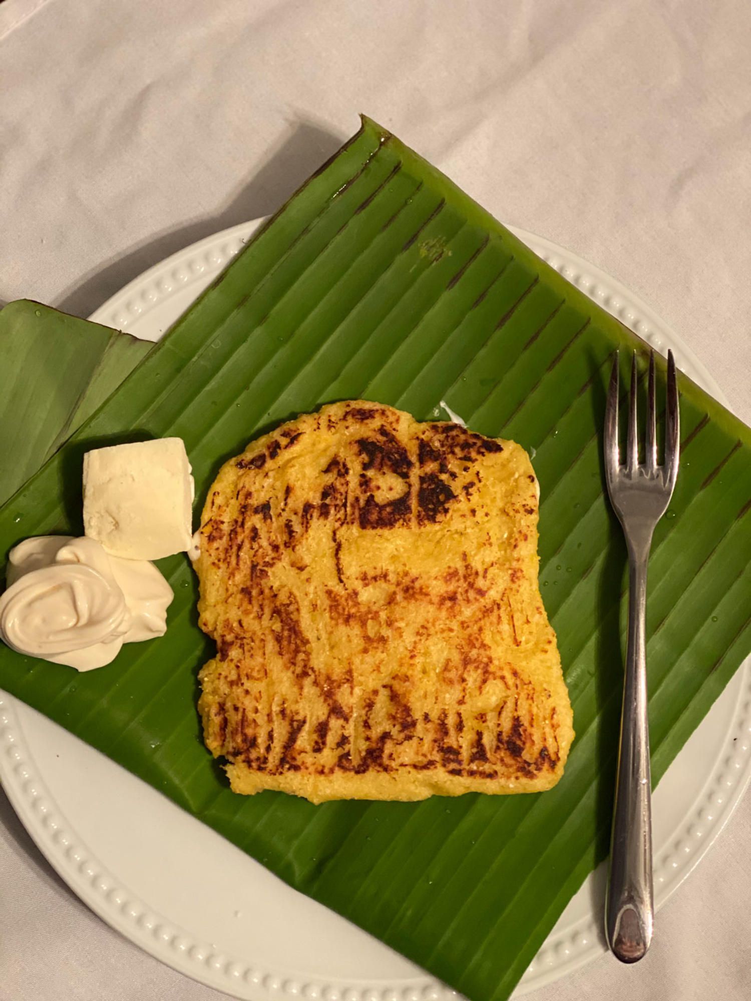 Arepa on a banana leaf, with cheese and a fork.