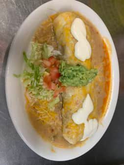 Burrito dish with cheese, sauce, guacamole, lettuce, tomato, and sour cream on a white plate.