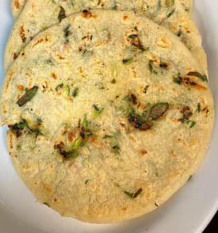 Round, flatbread with green herbs, stacked on a white plate.