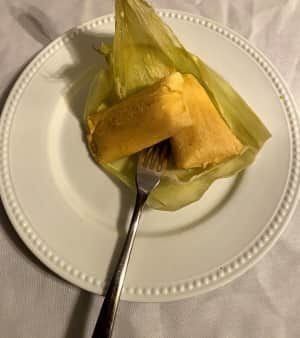 Tamales on a plate with a fork. Yellow corn husk, savory filling.