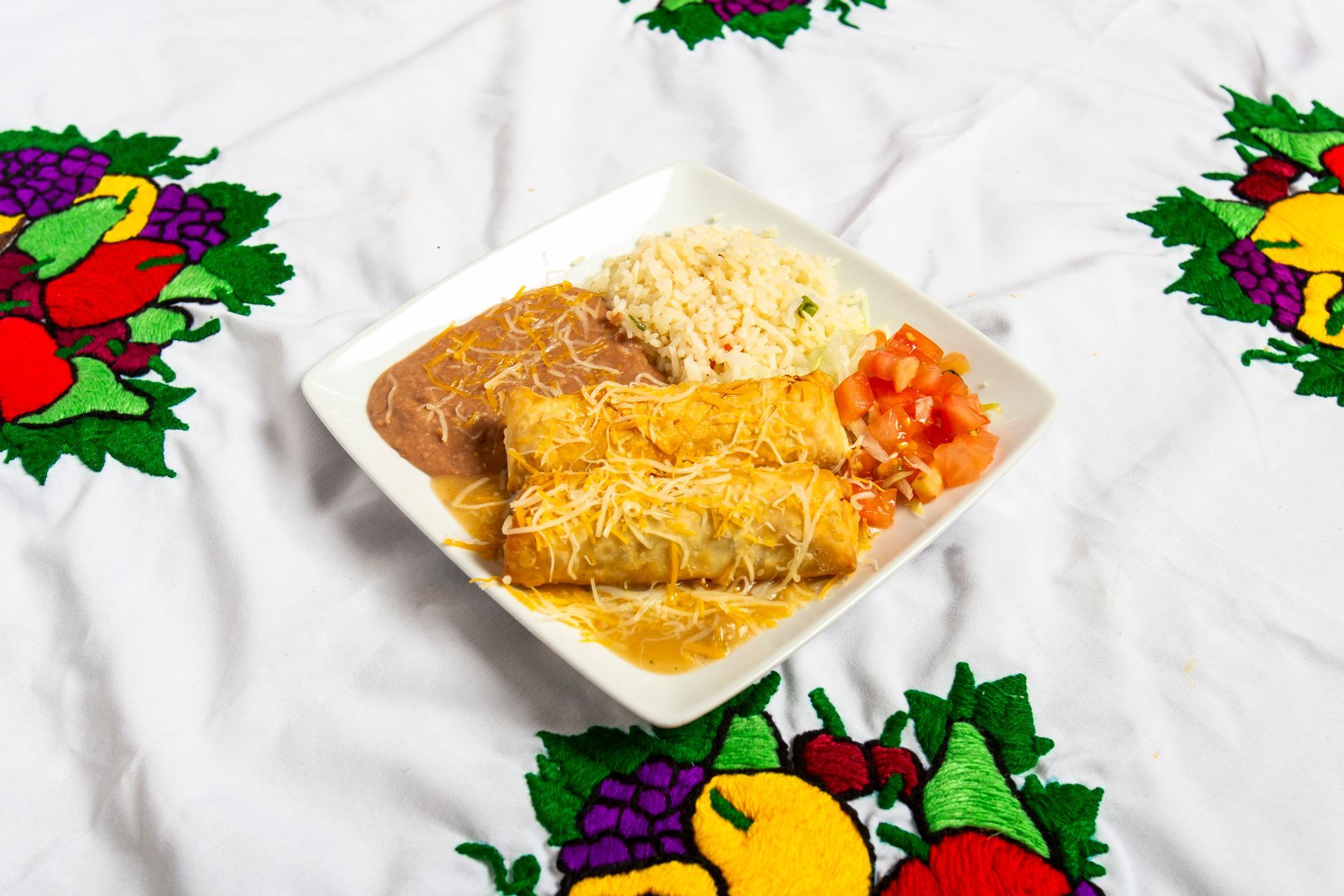 Mexican food plate: burritos with cheese, rice, beans, salsa on embroidered tablecloth.