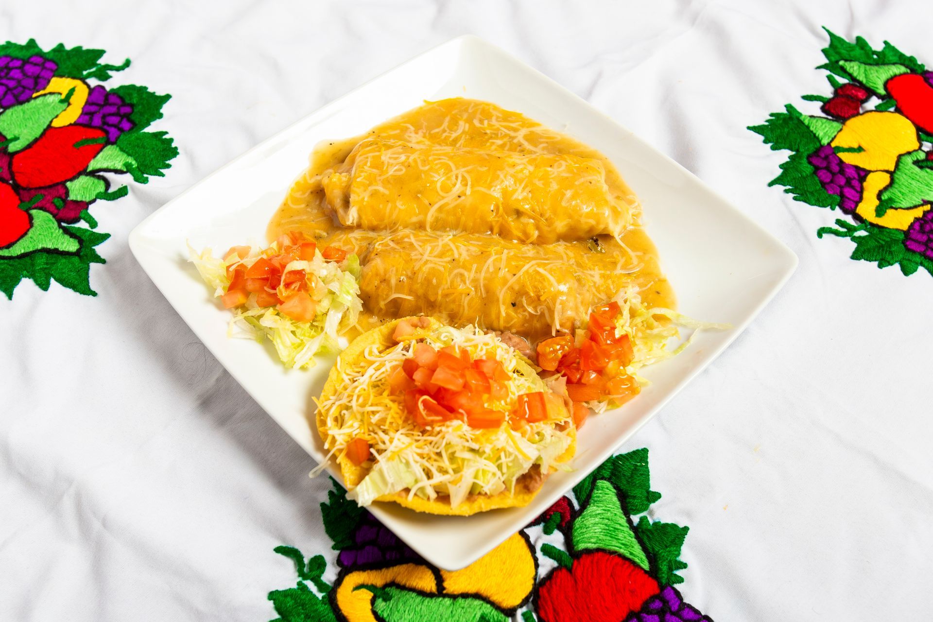 Plate of Mexican food: pupusas, topped with shredded cheese, salsa, and coleslaw, on embroidered tablecloth.