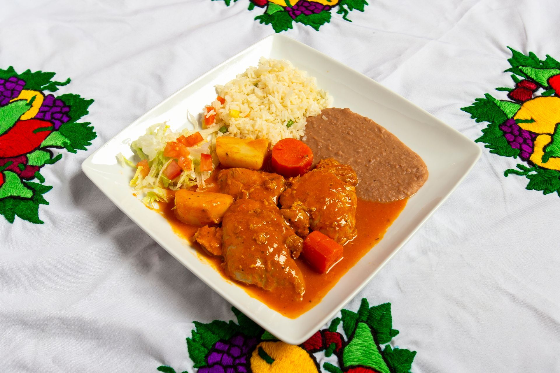 Plate with meat stew, rice, and beans on a decorated tablecloth.