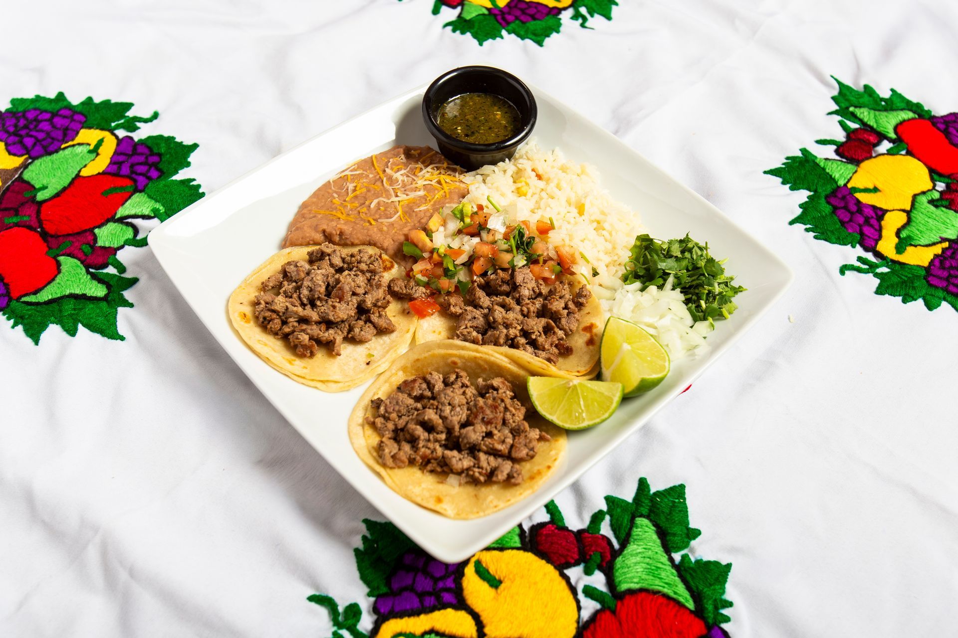 Tacos with rice, beans, salsa, and lime on a white plate, served on a decorated tablecloth.
