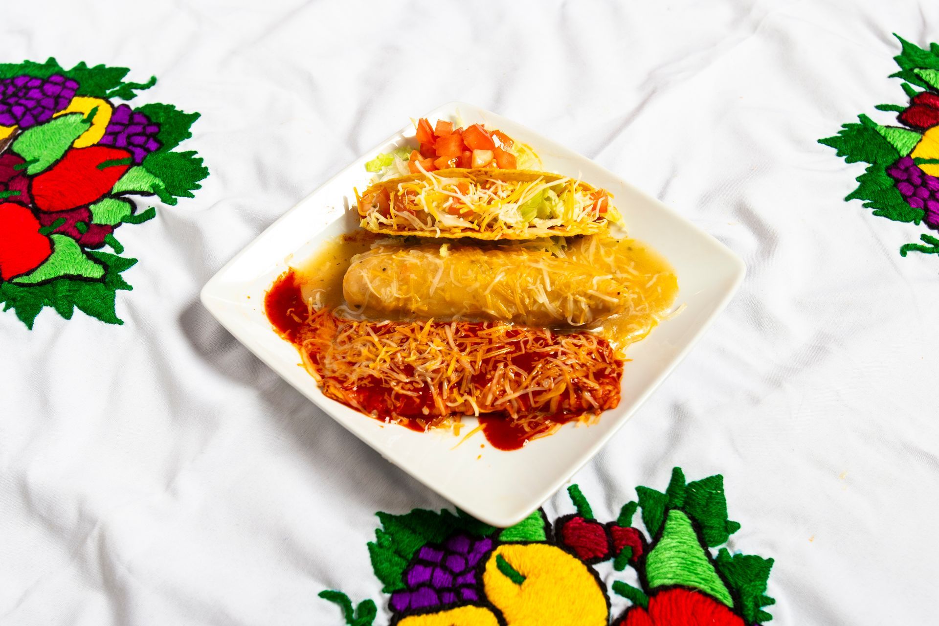 Plate of Mexican food with enchiladas, salsa, and cheese on a patterned tablecloth.