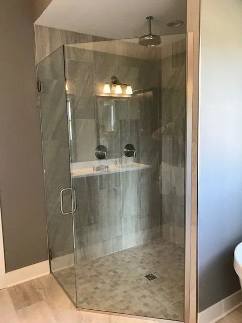 A modern walk-in shower with glass doors and grey tile walls, light wood-look flooring.