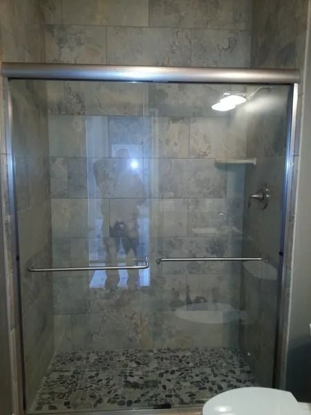 Shower with sliding glass doors, pebble floor, and tiled walls.