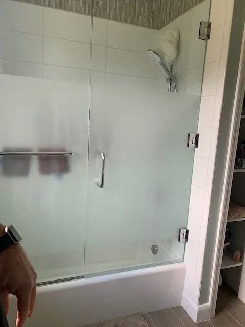 Frosted glass shower door with silver hardware in a tiled bathroom.