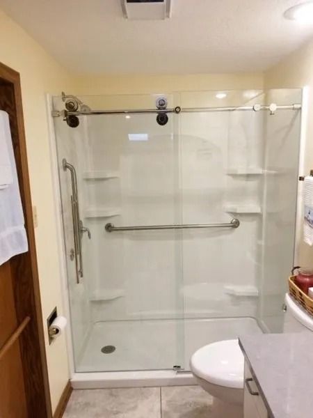 Bathroom with white shower stall, grab bars, sliding glass doors, toilet.