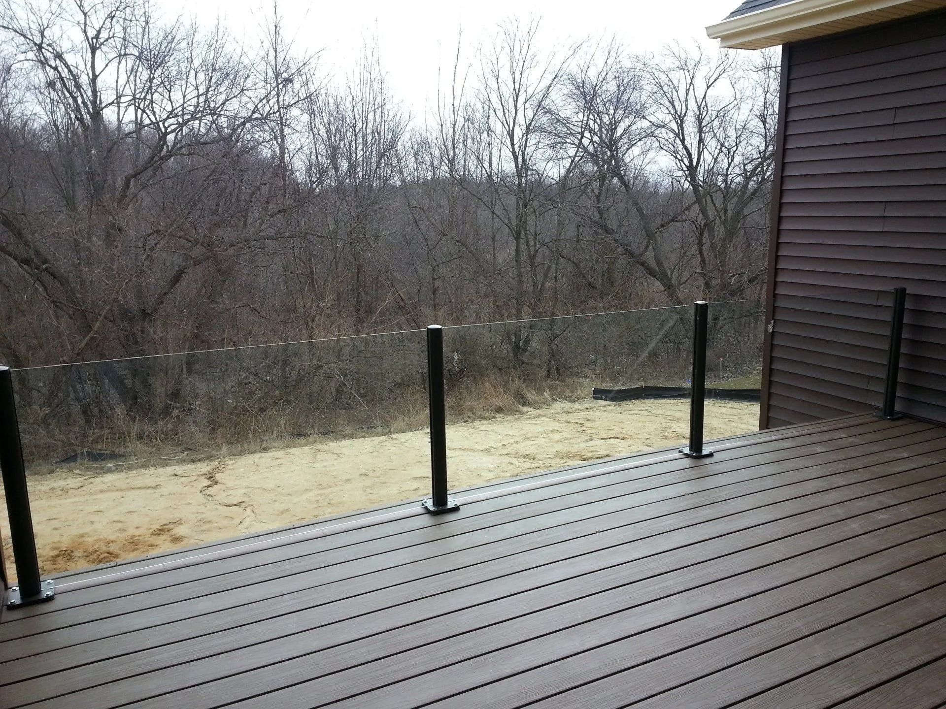 Deck with black posts and transparent railing overlooking trees and a brown-sided building.