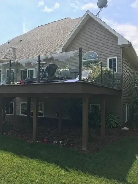 Back of a house with a deck. Deck has glass railings. House has gray siding and a satellite dish.