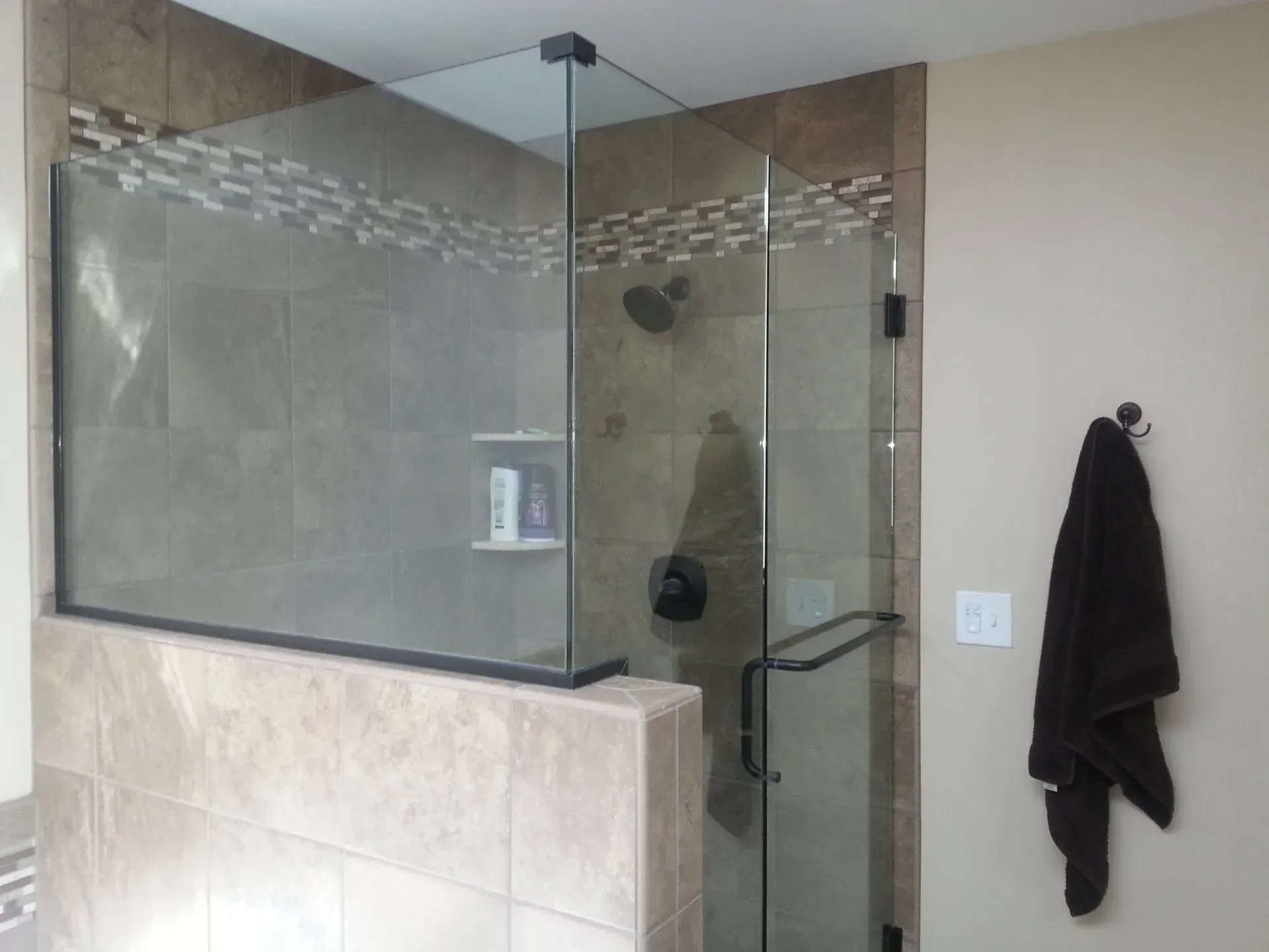 Glass shower enclosure with beige tile walls and a mosaic border. A dark towel hangs on the wall.