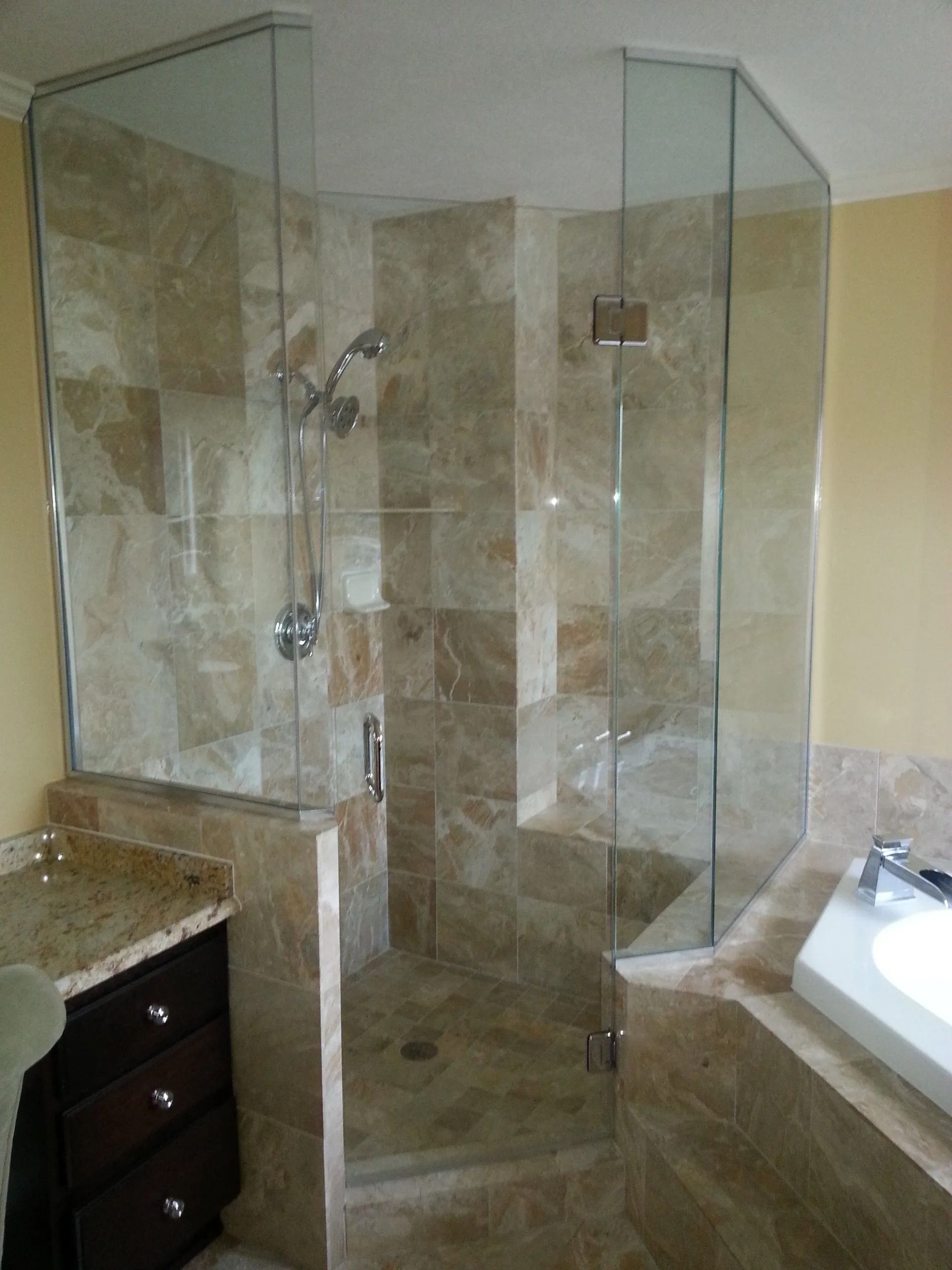 Shower with glass doors and beige tile walls. Features include a handheld shower head and a built-in bench.