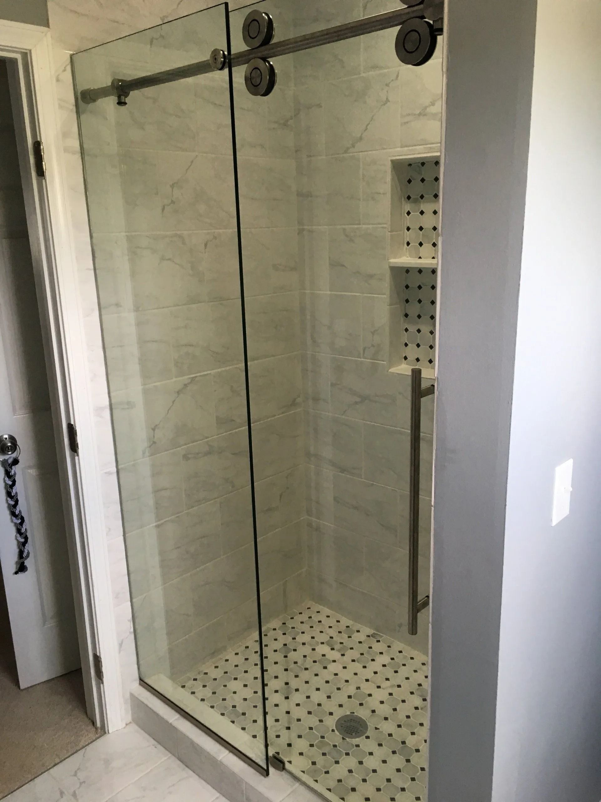 Shower with sliding glass doors, white tile walls, a built-in shelf, and a black and white tiled floor.