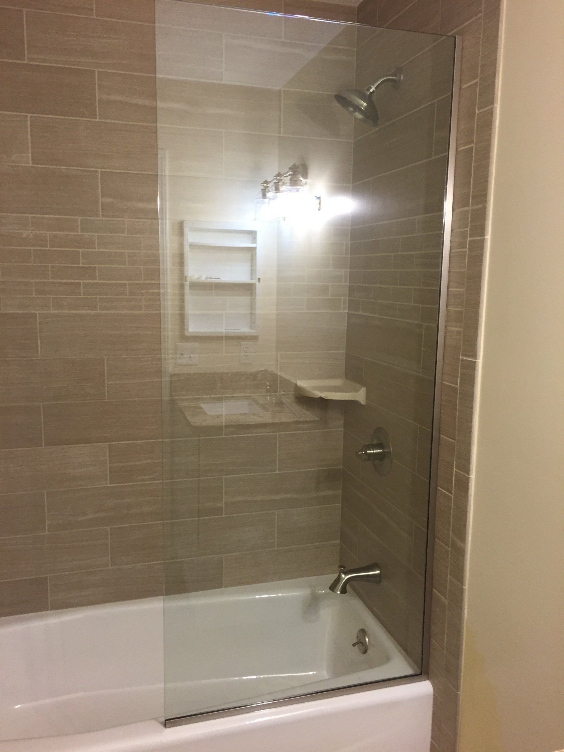 Bathroom with beige tiled walls, a white tub, and a glass shower door.