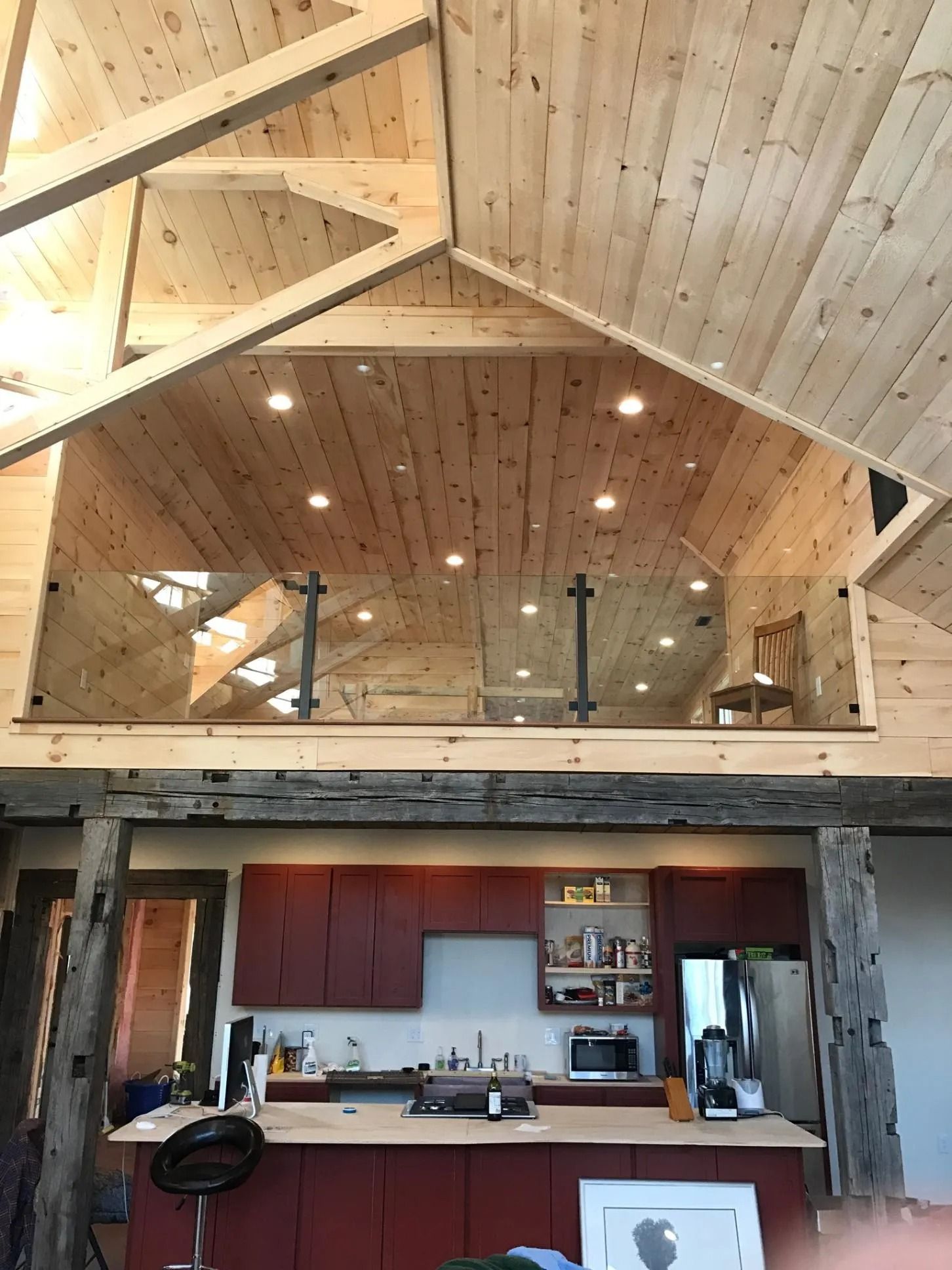 Interior view of a rustic home with a kitchen and loft. Wooden beams, red cabinets, and glass railing.