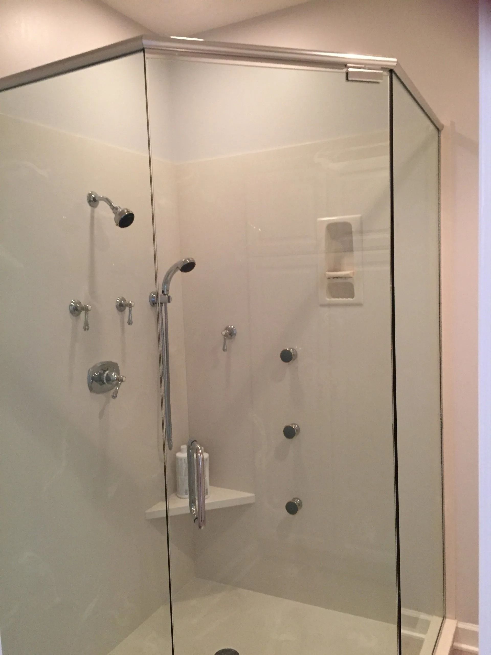Glass-enclosed shower with multiple showerheads and jets against a white wall.