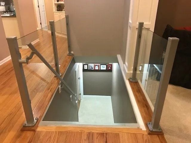 Staircase with glass and metal railing, leading down. Wooden floors and neutral-colored walls.