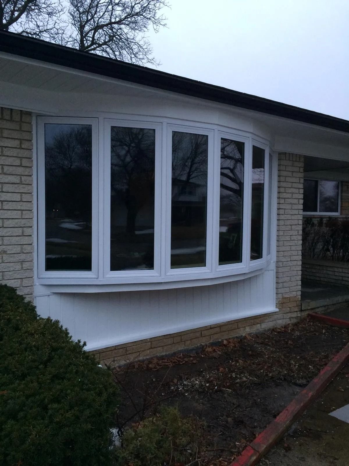 Bay window with white trim on a brick house. Overcast sky reflected in dark windows.