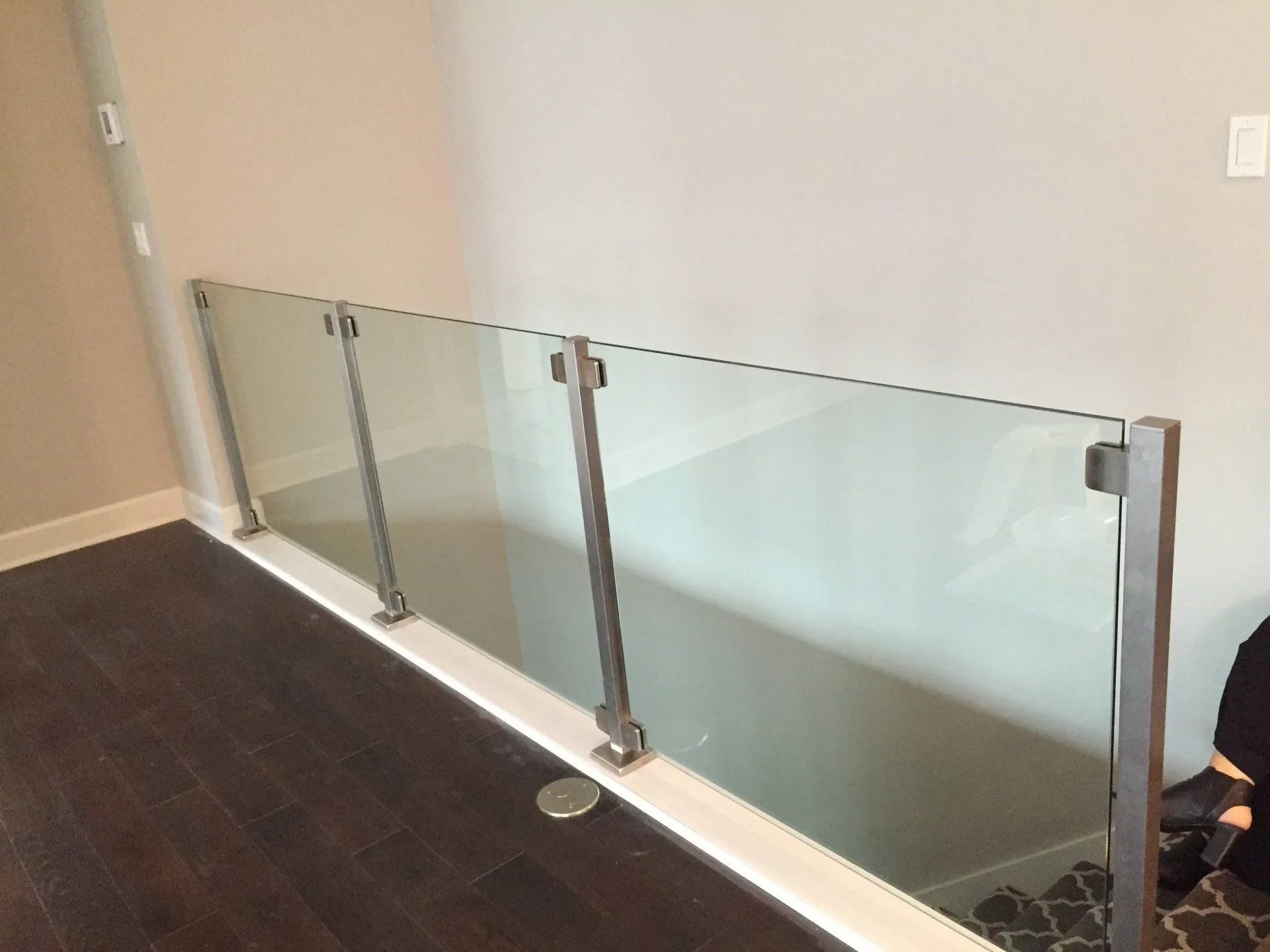 Glass and metal railing along a staircase. Brown flooring, light-colored walls.