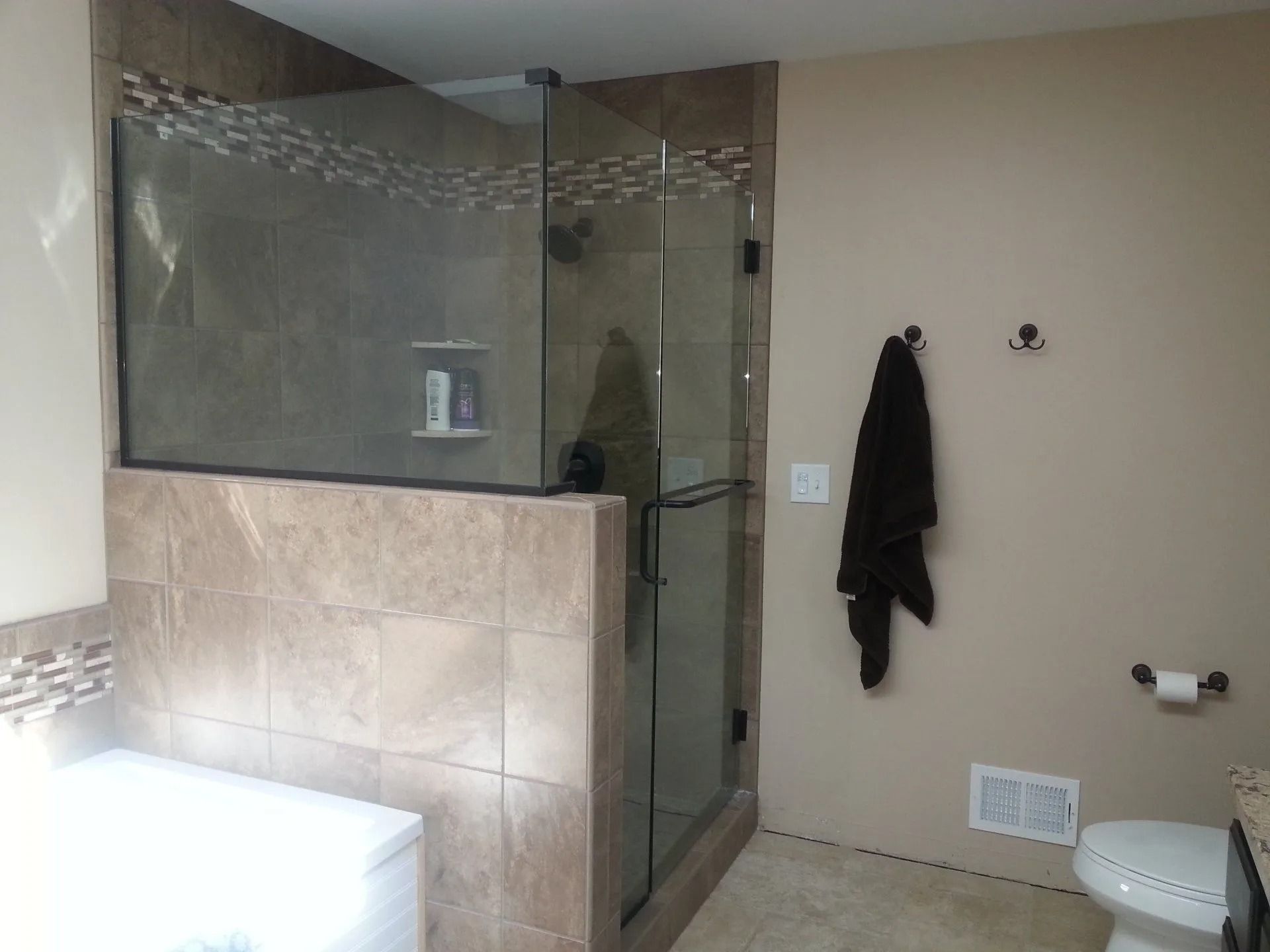 Bathroom with a glass shower enclosure and tiled walls. A dark towel hangs from hooks.
