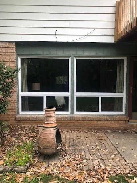 Two white-framed windows with panes set in a green trim, above brick. An old terracotta pot sits in front.