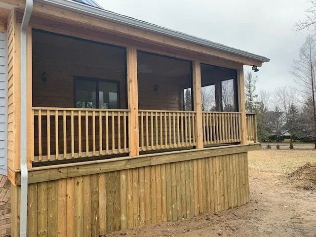 Screened-in wooden porch attached to a house with a railing, featuring screens, and a natural wood tone.