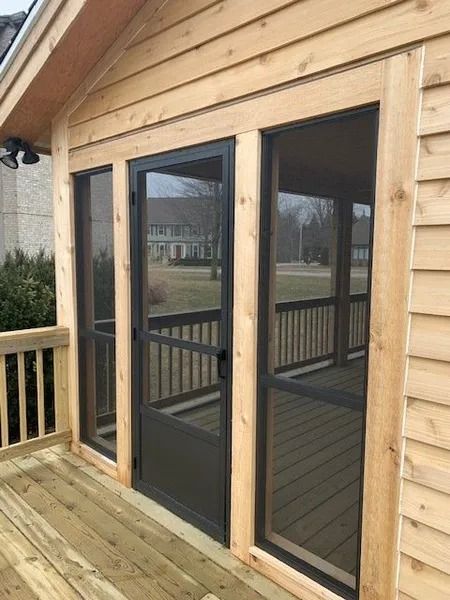 Screened porch with wooden deck and cedar siding. Dark gray screen door and window frames.