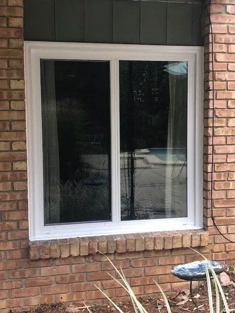 White-framed window on a brick building with a dark-colored top and landscaping below.
