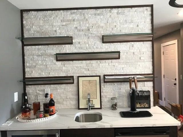 Bar area with white stone wall, floating shelves, sink, tap, and drinks.
