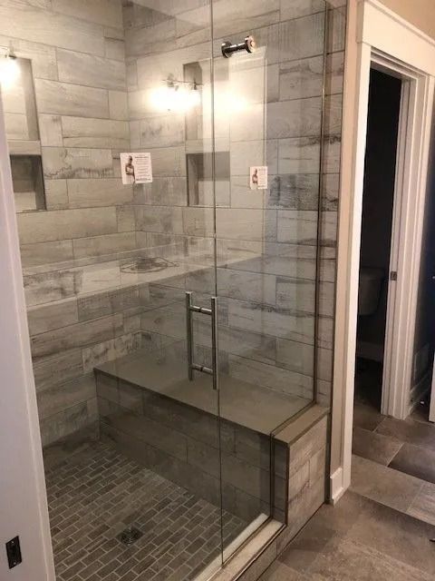 Shower with glass door, gray tile walls and floor, built-in bench, and showerhead.