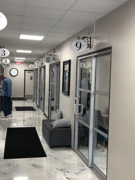 Hallway with numbered doors. A person stands near door 3. Black mats on marble floor.