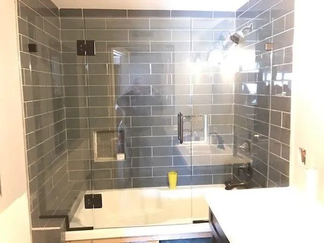 Glass-walled shower with gray subway tile. Features a built-in bench, shelf, and chrome fixtures.