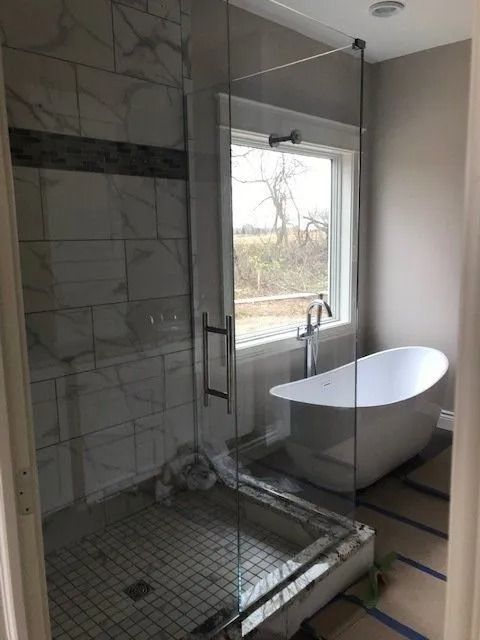 Modern bathroom with a glass shower, soaking tub, and window.