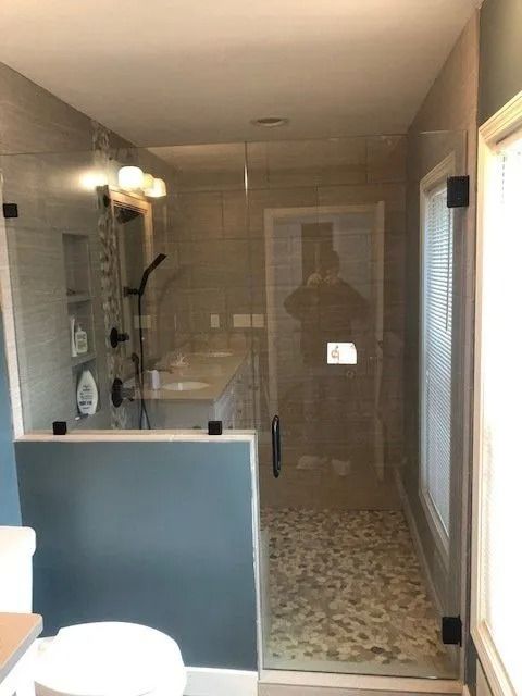 Glass shower with black hardware, pebble floor, and blue accent wall.