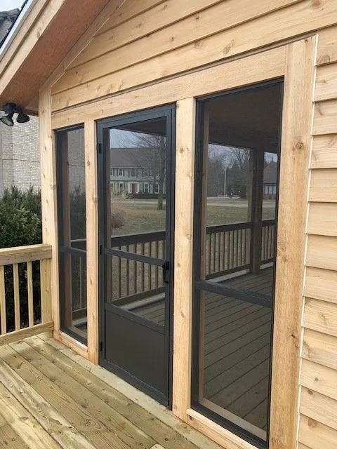 Screened porch with wooden siding, door, and windows. Brown door frame and porch railing. Green lawn in the background.