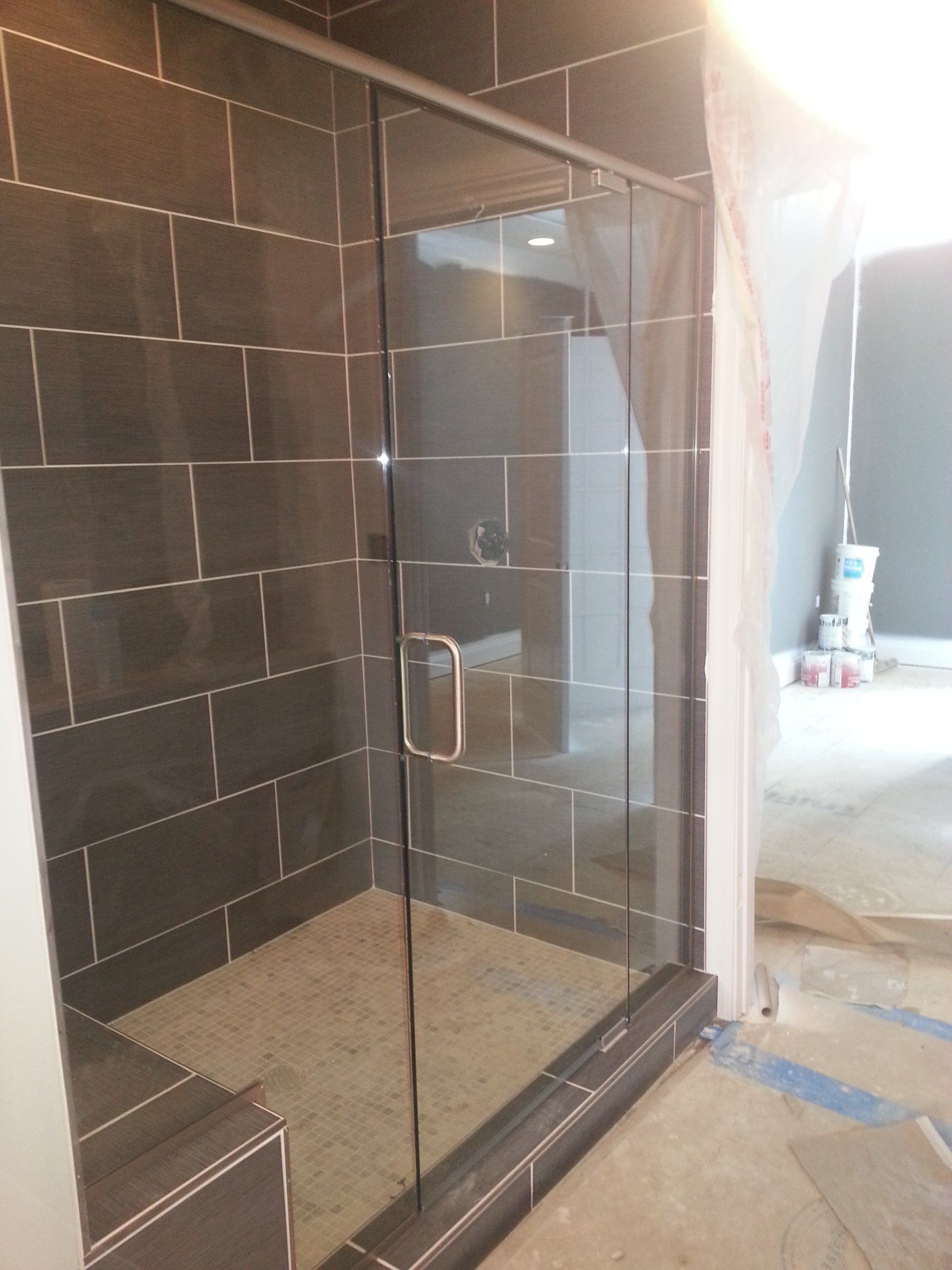 Glass shower enclosure with dark tiled walls, in a room under construction.