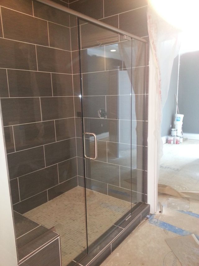 Glass shower enclosure with dark tiled walls, in a room under construction.
