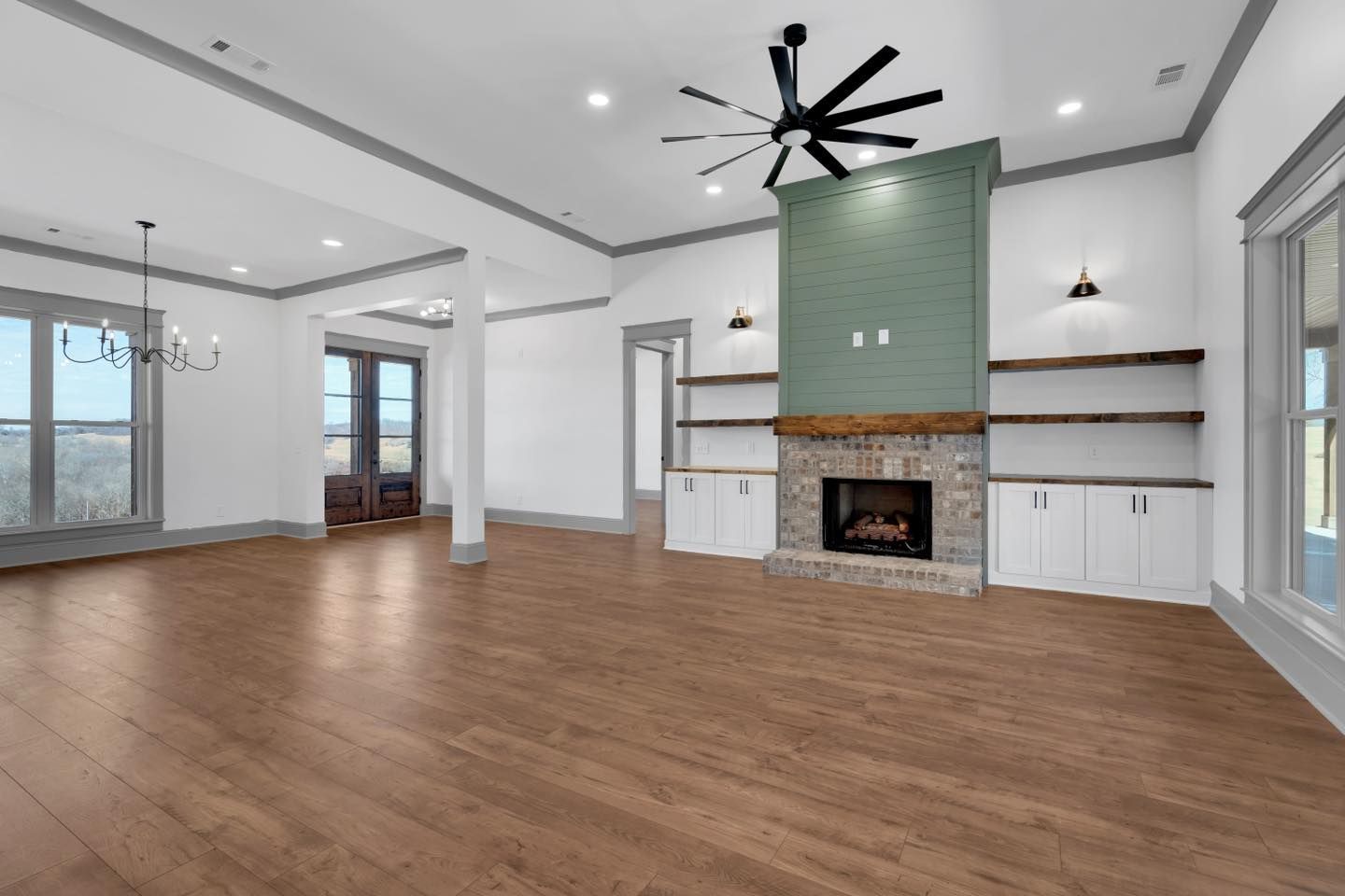 An empty living room with hardwood floors, a fireplace, and a ceiling fan.